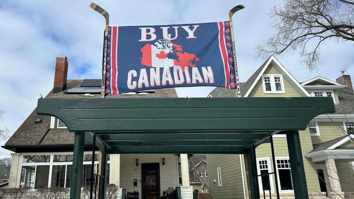 A banner reading "Buy Canadian", in response to U.S. President Donald Trump's 25% tariffs on goods from Canada, is held aloft by a pair of hockey sticks in front of a house