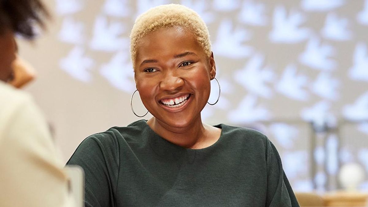 A Black woman smiling while looking at a person only partially shown