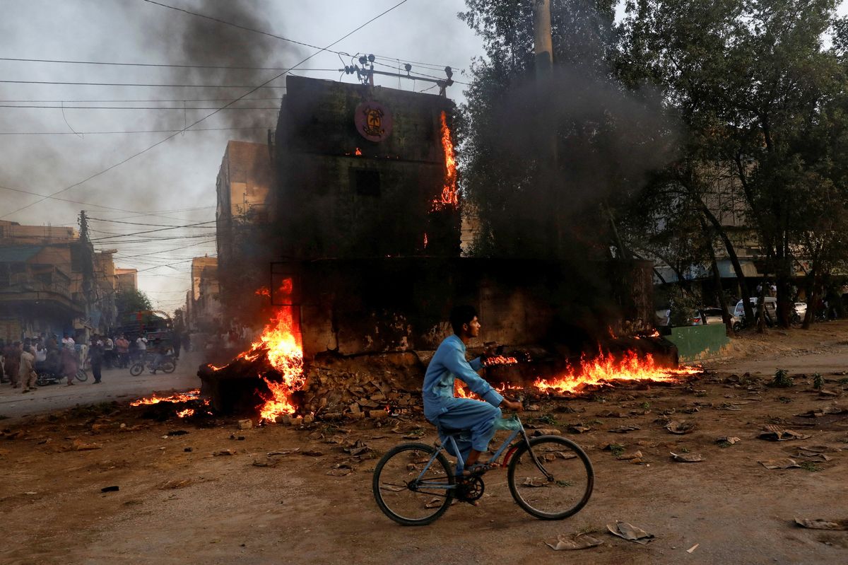 A boy rides past a paramilitary check post, that was set afire by the supporters of Pakistan's former Prime Minister Imran Khan