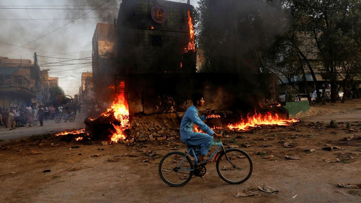A boy rides past a paramilitary check post, that was set afire by the supporters of Pakistan's former Prime Minister Imran Khan