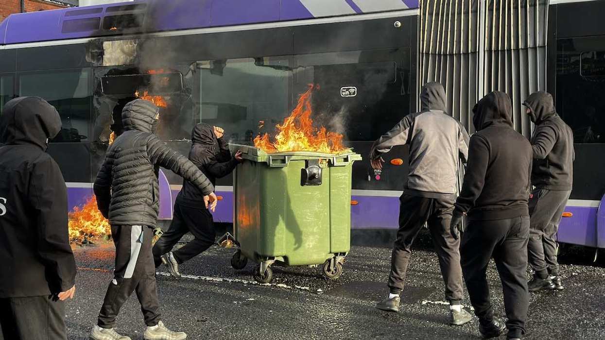 A bus being set on fire by protestors holding a garbage bin on fire in east Belfast