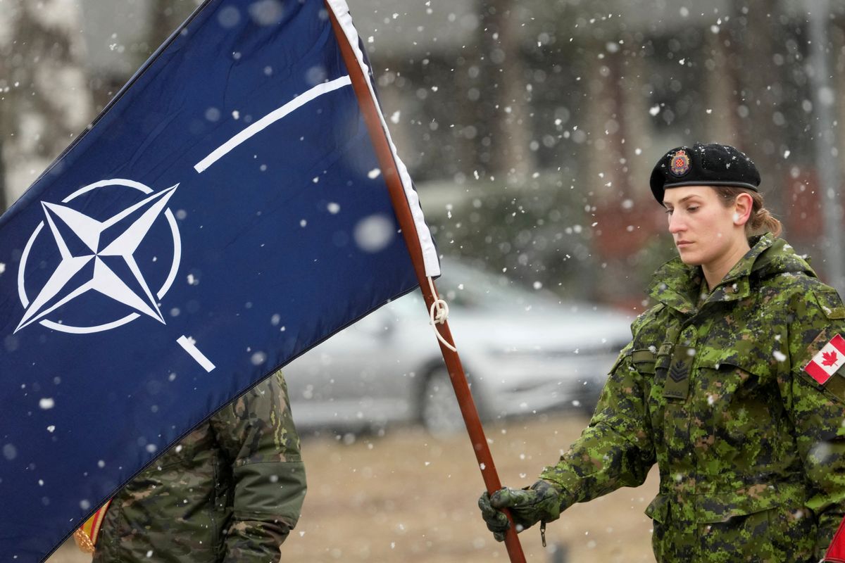 A Canadian soldier holds a flag as they wait for the arrival of PM Justin Trudeau along with NATO Secretary-General Jens Stoltenberg in Adazi, Latvia.