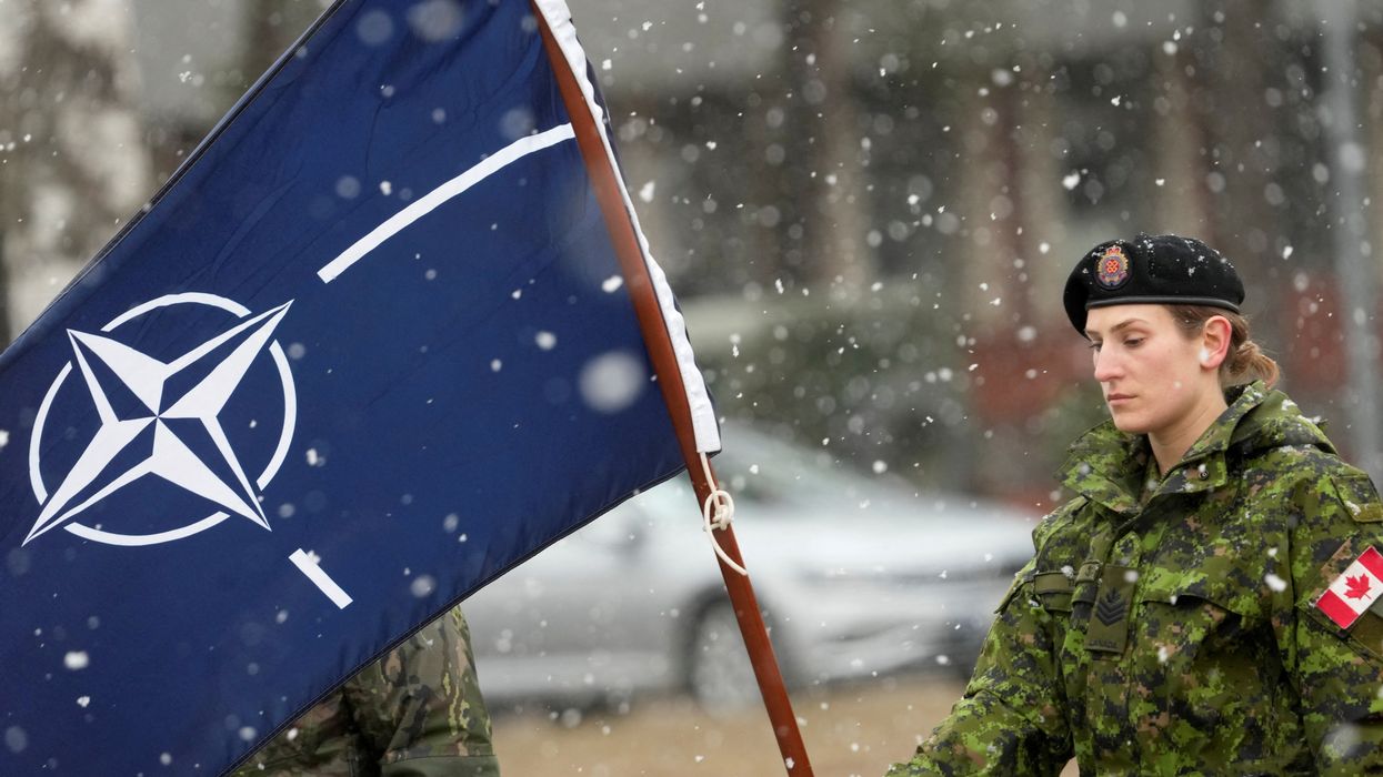 A Canadian soldier holds a flag as they wait for the arrival of PM Justin Trudeau along with NATO Secretary-General Jens Stoltenberg in Adazi, Latvia.