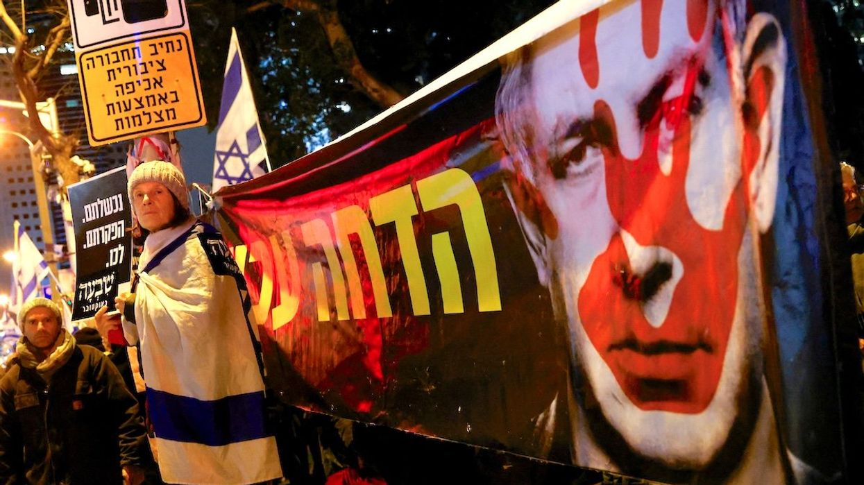 A demonstrator stands next to a banner with an image of Israeli Prime Minister Benjamin Netanyahu as she attends a rally in Tel Aviv to demand an immediate cease-fire in Gaza on Jan. 27, 2024.