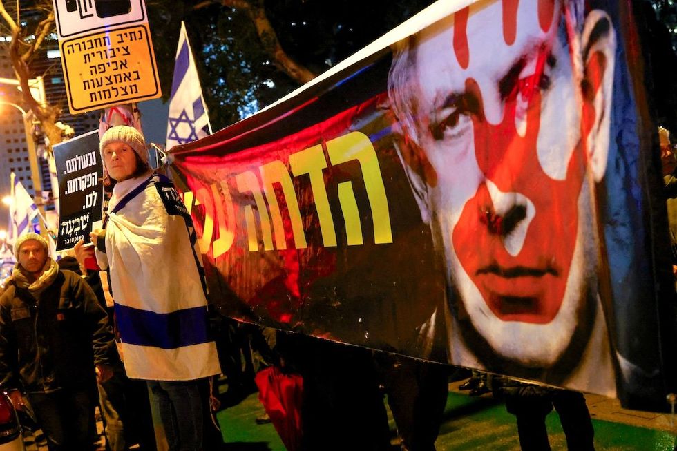 A demonstrator stands next to a banner with an image of Israeli Prime Minister Benjamin Netanyahu as she attends a rally in Tel Aviv to demand an immediate cease-fire in Gaza on Jan. 27, 2024.
