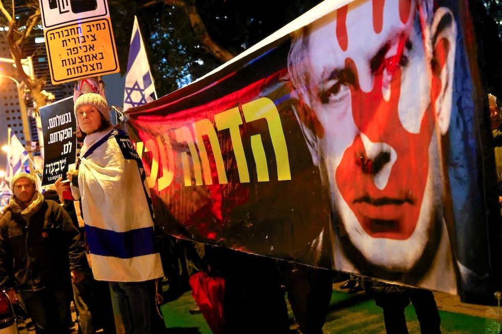 ​A demonstrator stands next to a banner with an image of Israeli Prime Minister Benjamin Netanyahu as she attends a rally in Tel Aviv to demand an immediate cease-fire in Gaza on Jan. 27, 2024. 