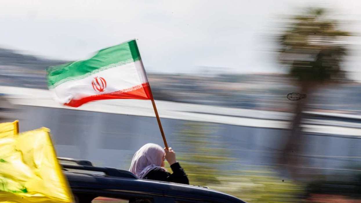 A displaced woman holds an Iranian flag from the sunroof of a moving car