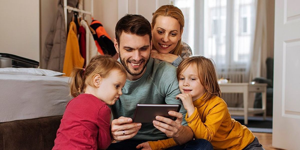 A father, his partner, and their two kids looking at an ipad and smiling
