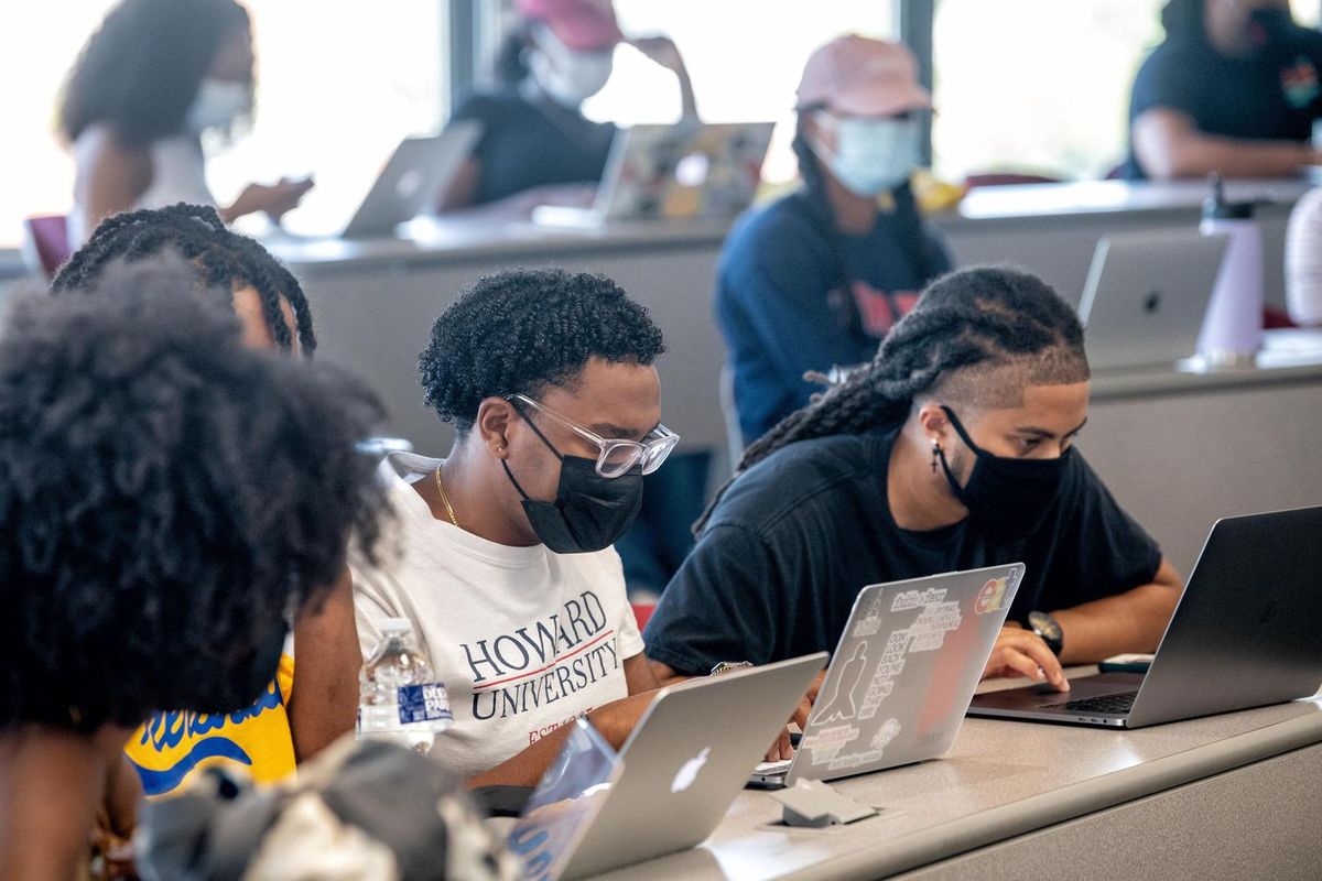 A group of students wearing COVID masks while working at laptops.