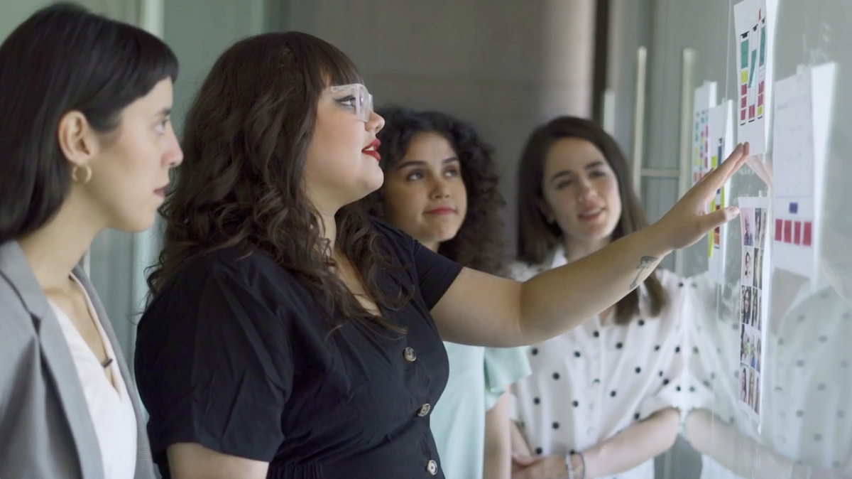 A group of young women looking together at images on a wall. 