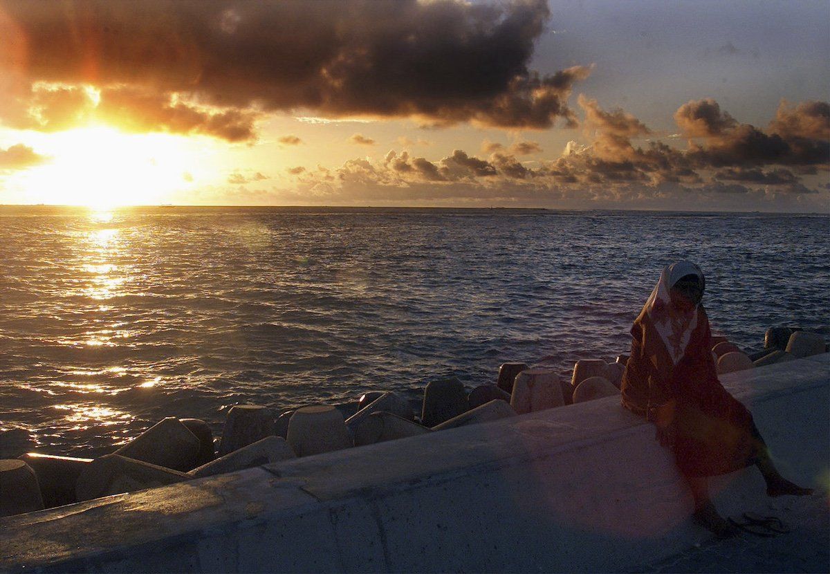 A Maldivian woman sits atop a section of a dyke built to protect the tiny island from the ravages of the sea during a sunrise in the Maldives capital Male in this July 12, 2001 file photo.