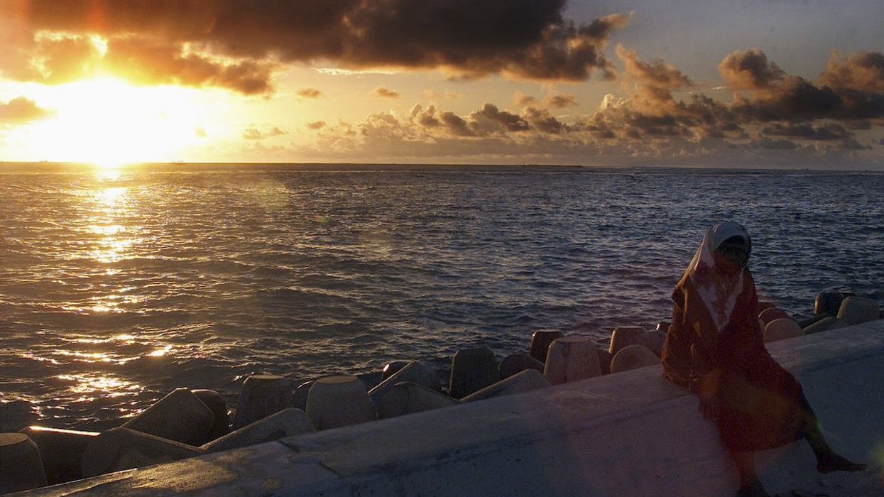 A Maldivian woman sits atop a section of a dyke built to protect the tiny island from the ravages of the sea during a sunrise in the Maldives capital Male in this July 12, 2001 file photo.