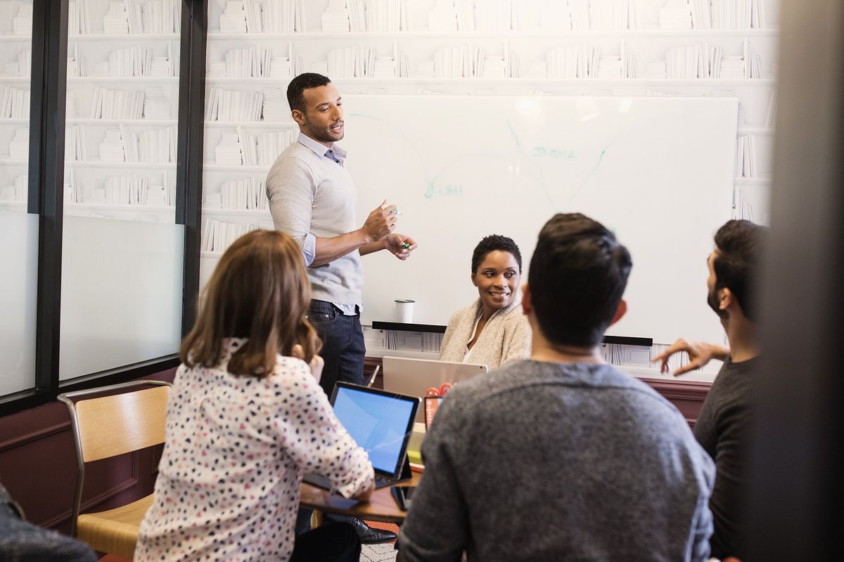 A man conducting a meeting with 4 other teammates