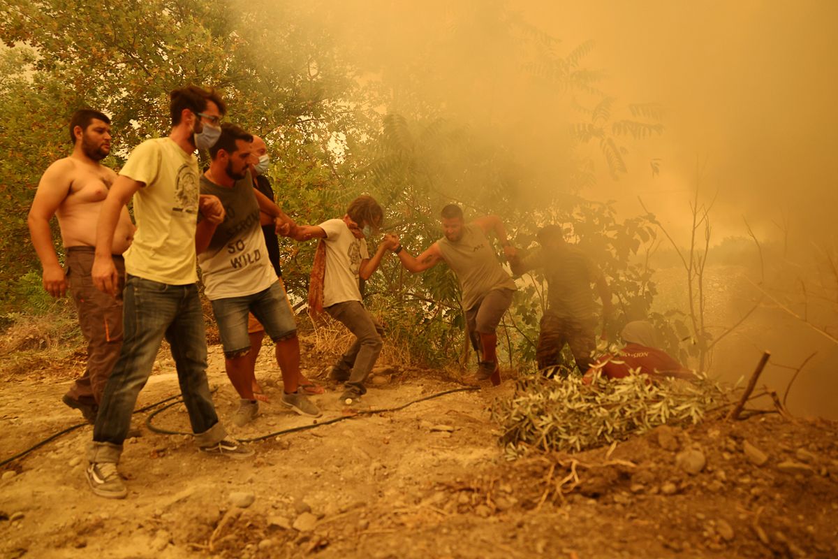 A man holding a hose is helped to climb a slope, as a wildfire burns in the village of Gouves, on the island of Evia, Greece, August 8, 2021.