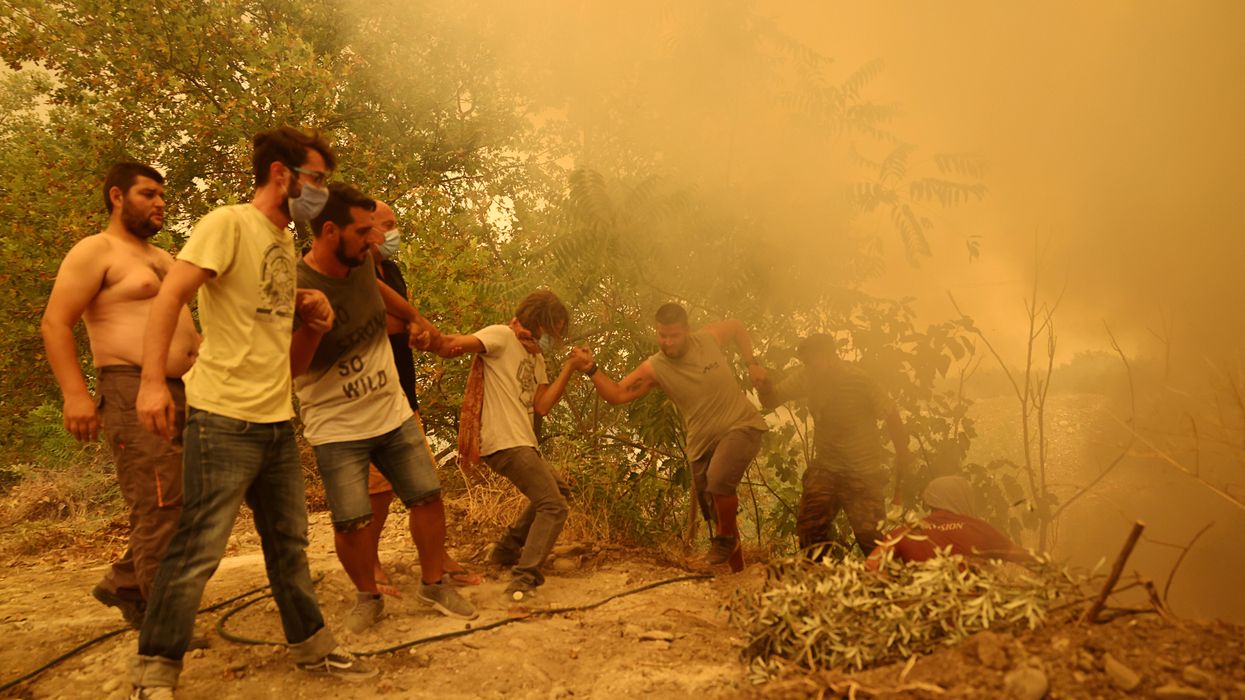 A man holding a hose is helped to climb a slope, as a wildfire burns in the village of Gouves, on the island of Evia, Greece, August 8, 2021.