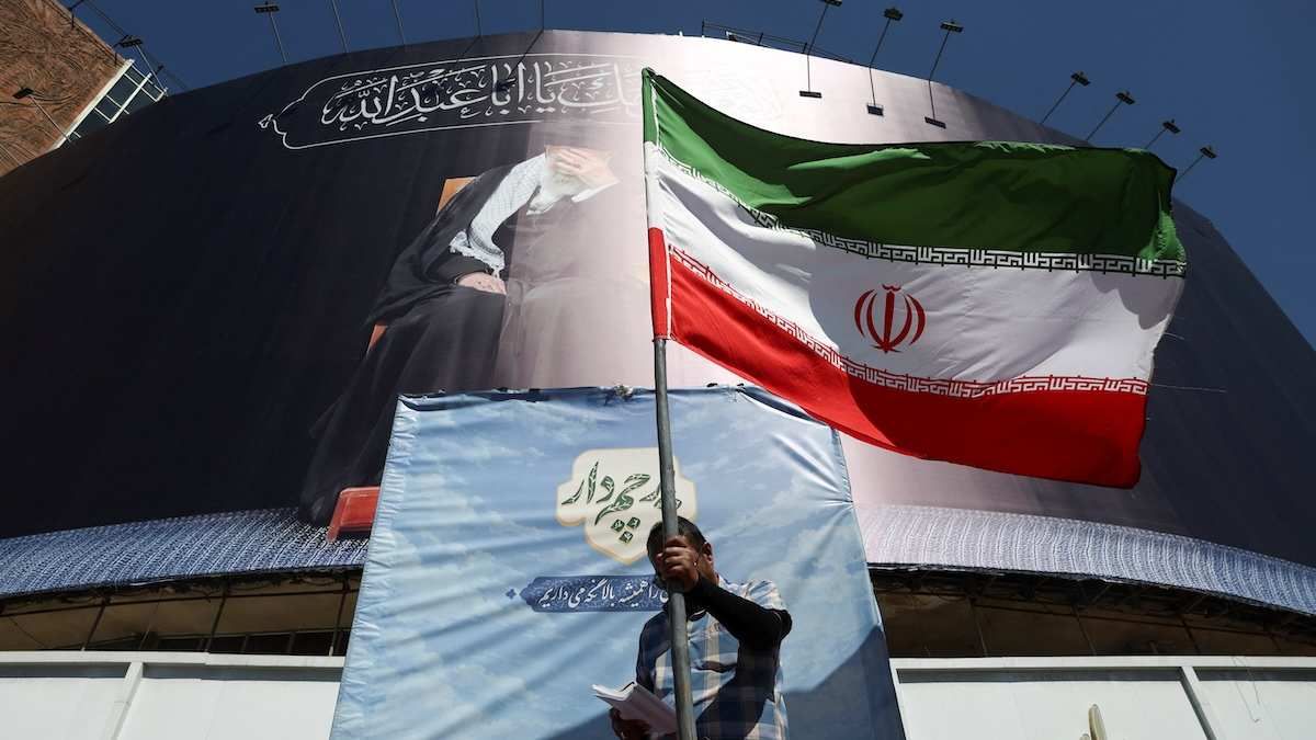 A man holds an Iranian flag on a street while reading a newspaper