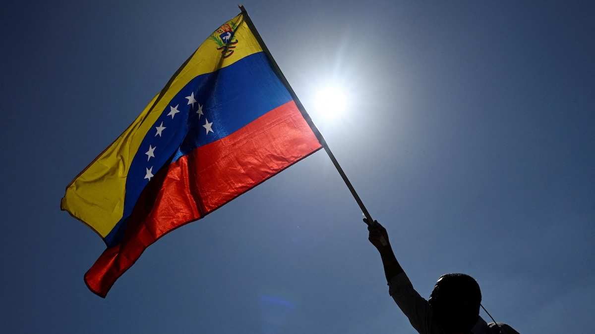 A man holds up a Venezuelan flag in front of the sun.