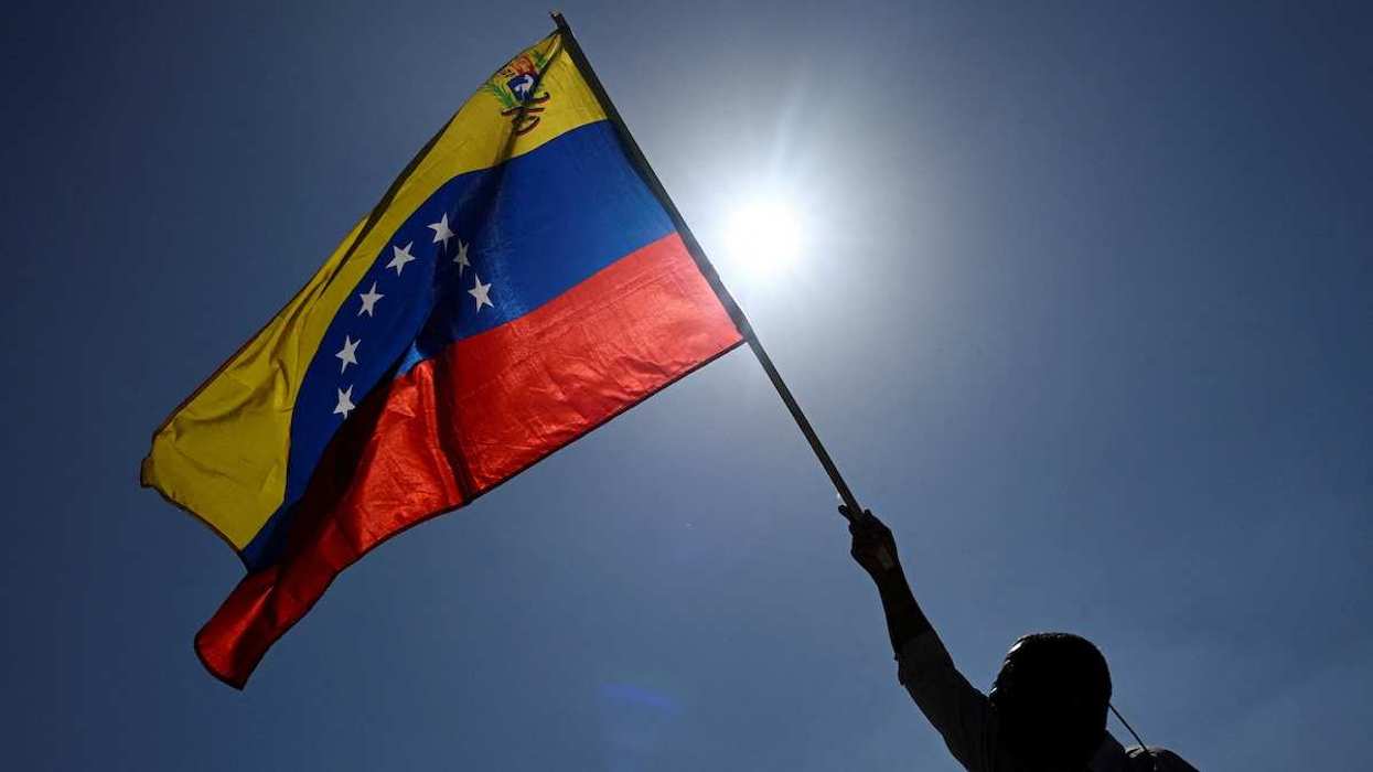 A man holds up a Venezuelan flag in front of the sun.