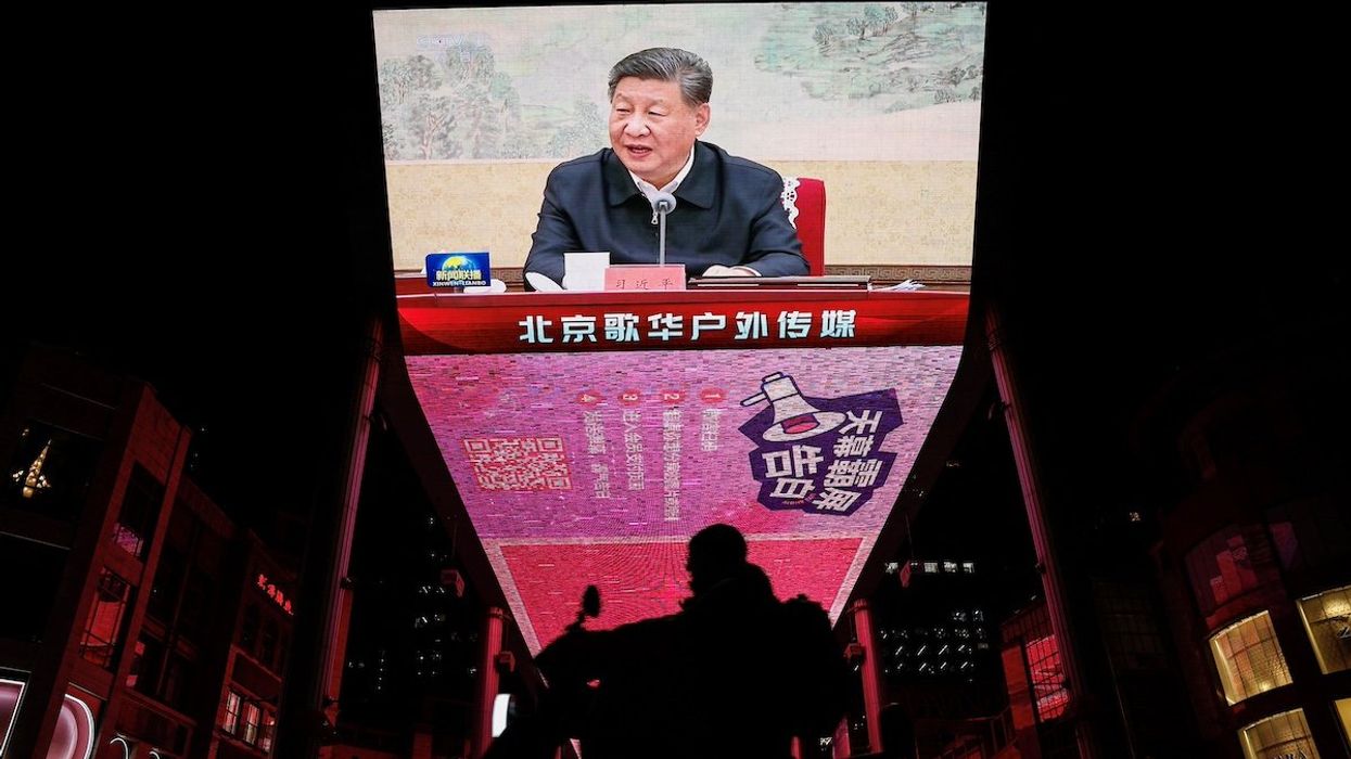 A man rides a scooter past a giant screen showing news footage of Chinese President Xi Jinping attending a Chinese Communist Party politburo meeting, in Beijing, China December 9, 2024.