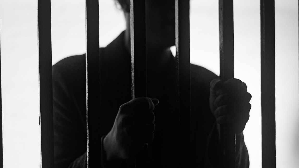 A man standing behind bars in a jail cell silhouetted.