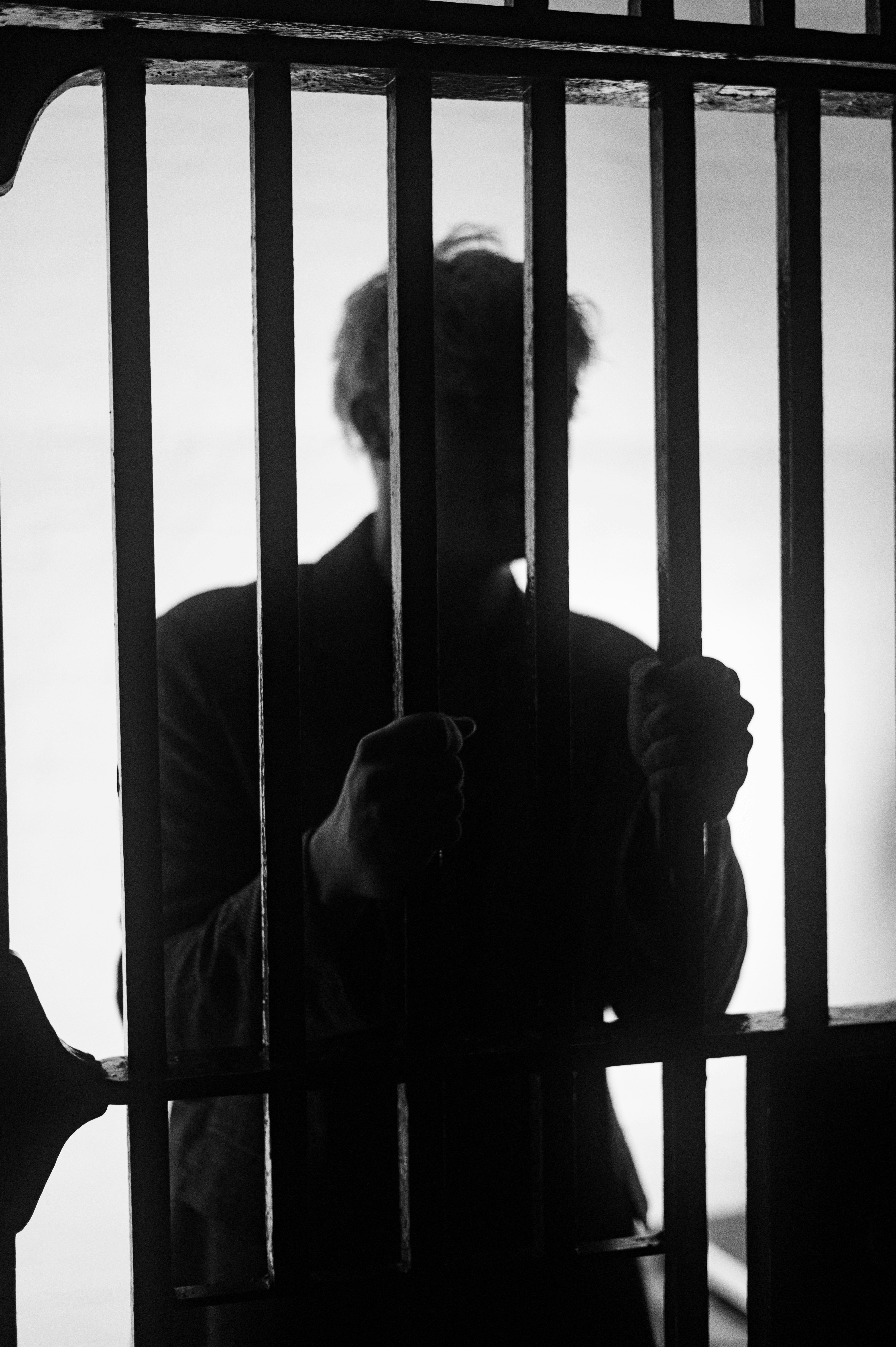 A man standing behind bars in a jail cell silhouetted.