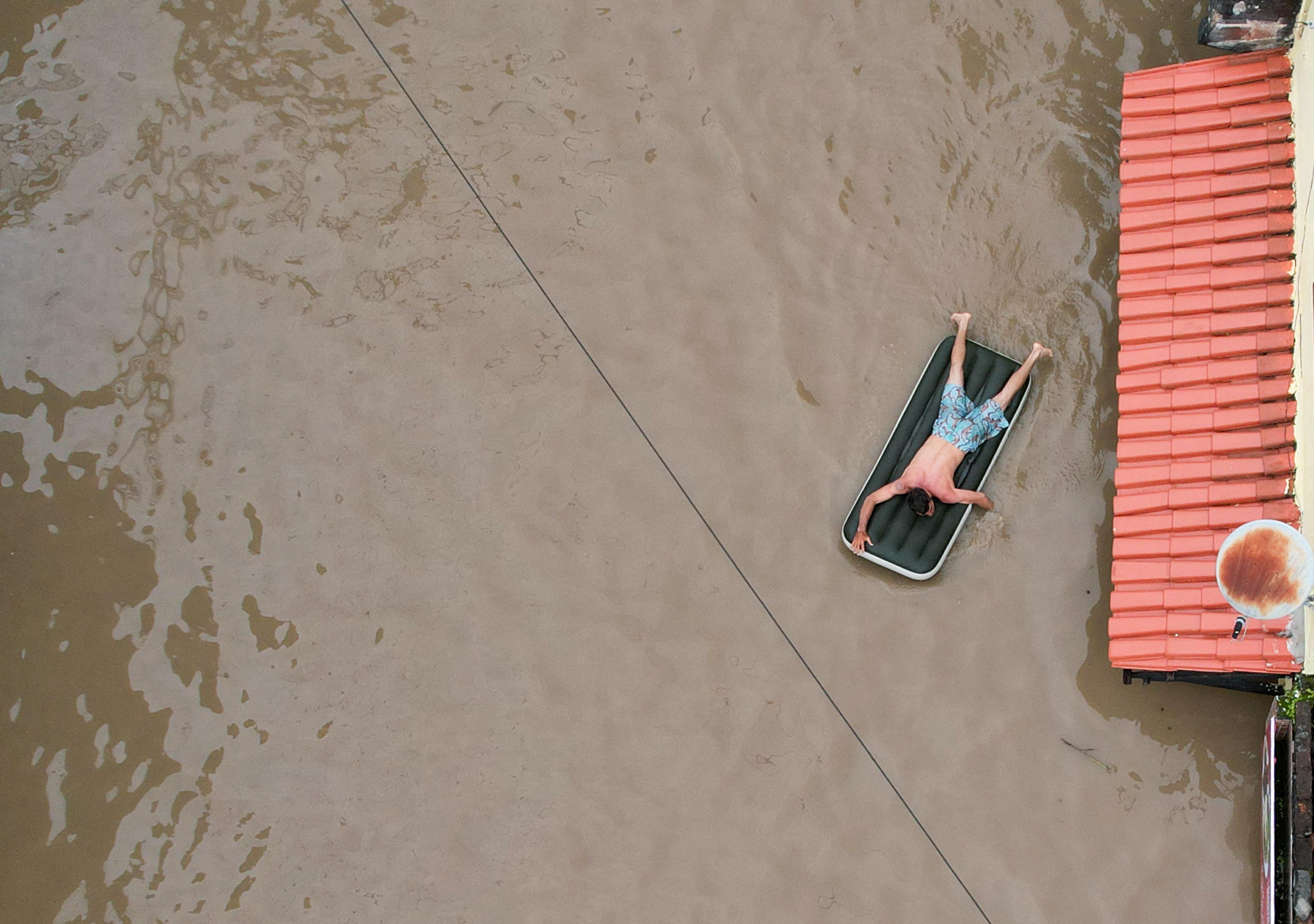 A man uses an inflatable mattress during flooding caused by the overflowing Cachoeira river in Itabuna, Bahia state, Brazil, December 26, 2021. Picture taken with a drone.