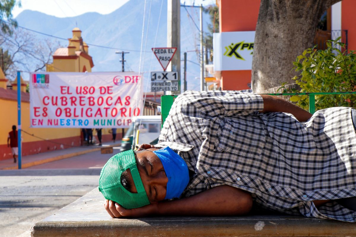 A man wearing a face mask sleeps at a park near a banner reading "The use of face masks is mandatory in our municipality", amid the coronavirus disease (COVID-19) pandemic, in Tlacolula de Matamoros, Oaxaca state, Mexico January 30, 2021.