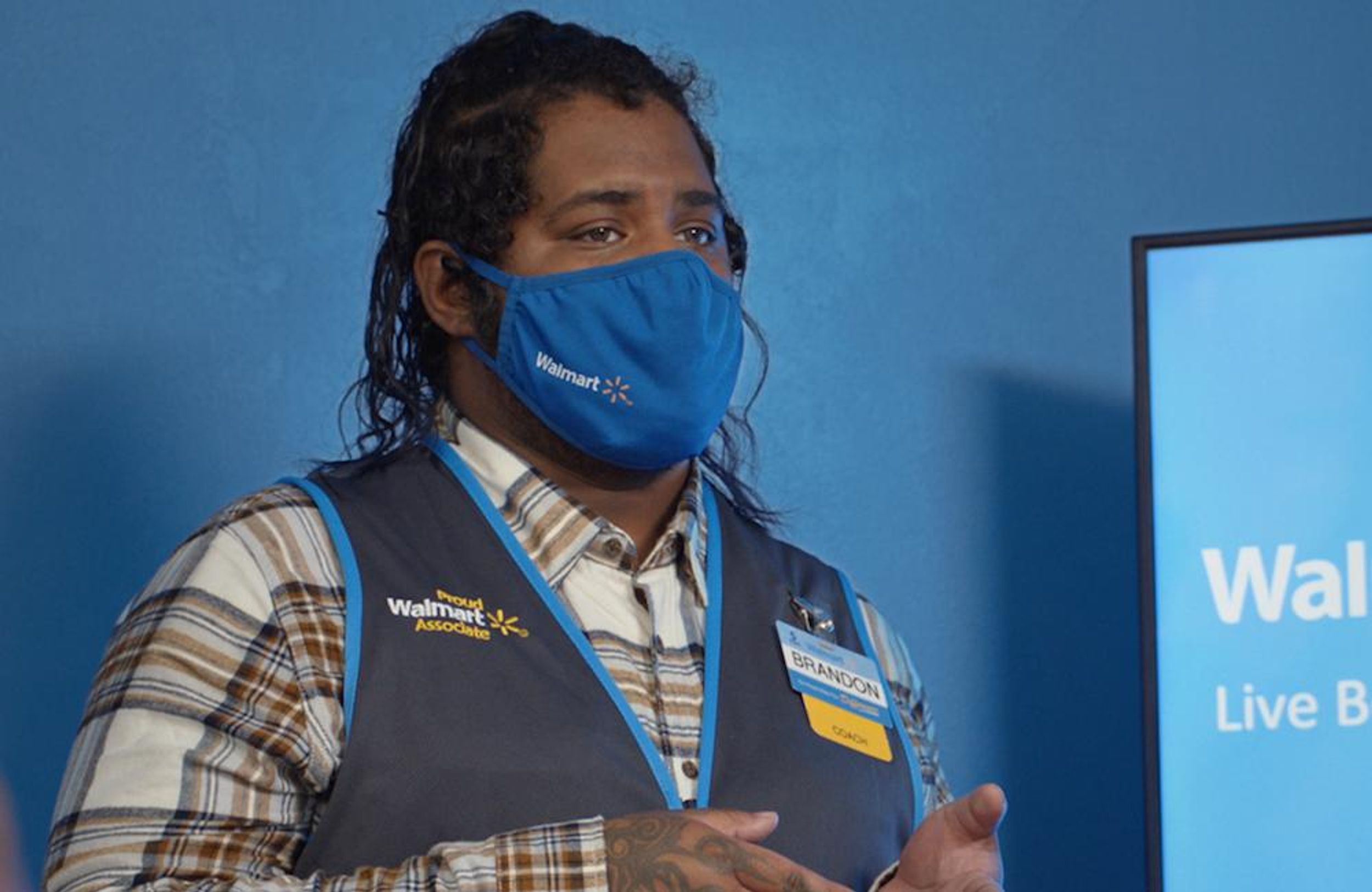 A masked Walmart employee giving a presentation in a room with blue walls