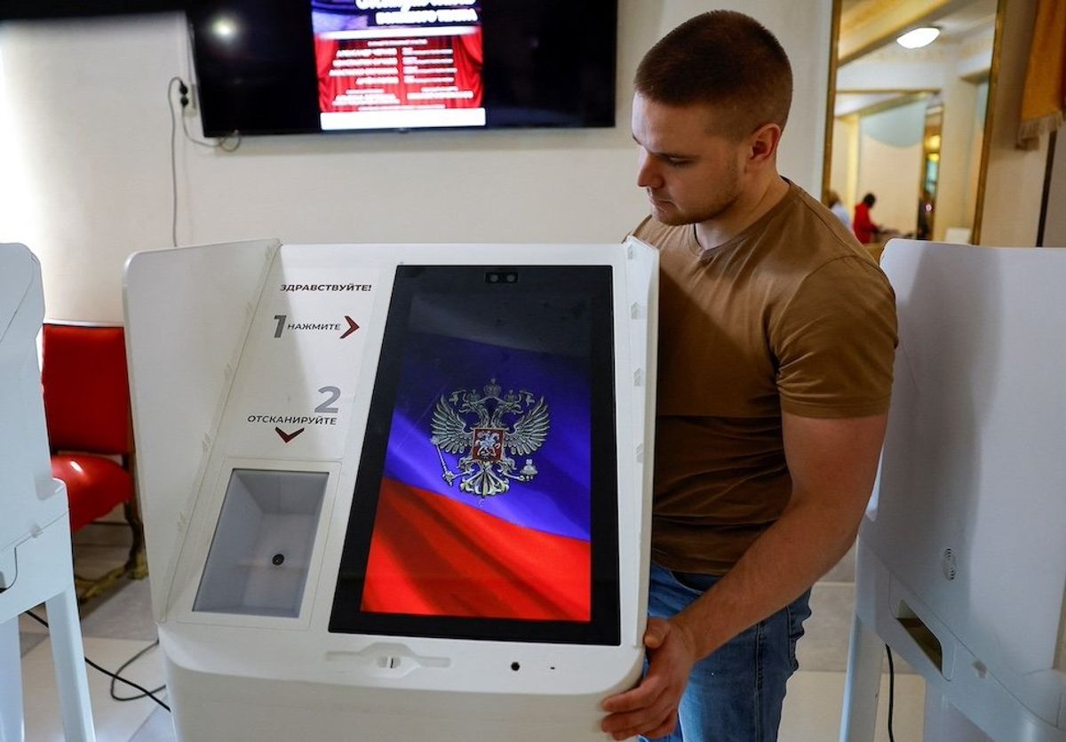 ​A member of a local electoral commission installs an electronic voting machine at a polling station during preparations for the presidential election, in Moscow, Russia, March 14, 2024. 
