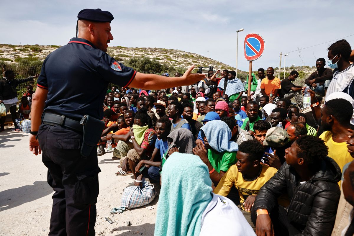 A member of the Carabinieri gestures towards migrants outside the hotspot, on the Sicilian island of Lampedusa, Italy, September 16, 2023.