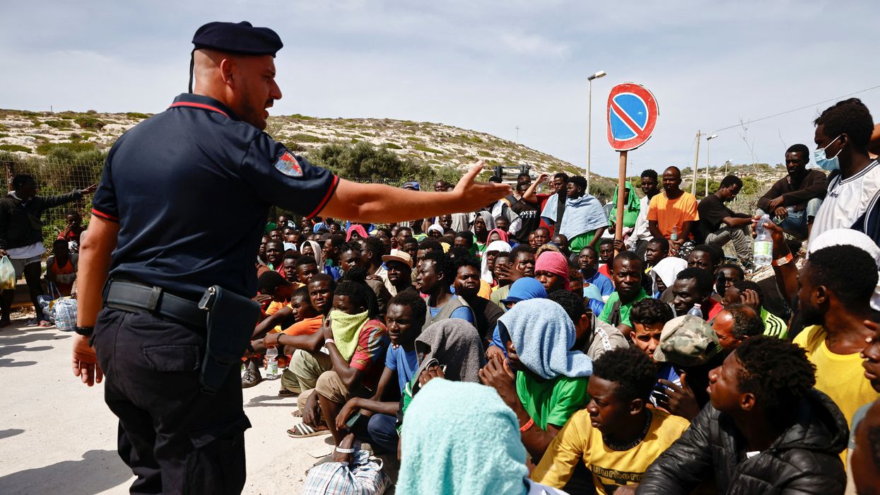 A member of the Carabinieri gestures towards migrants outside the hotspot, on the Sicilian island of Lampedusa, Italy, September 16, 2023.
