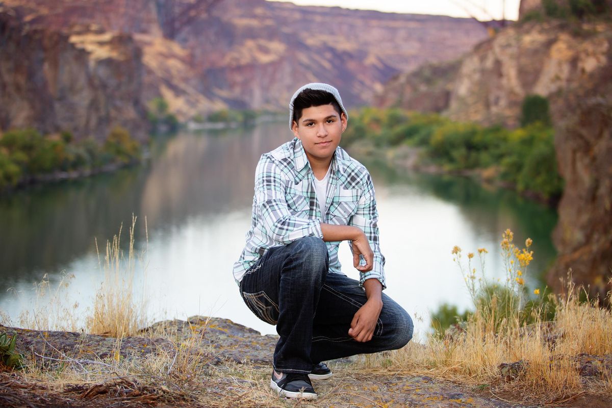 A Native American youth kneeling alongside a river canyon, grinning