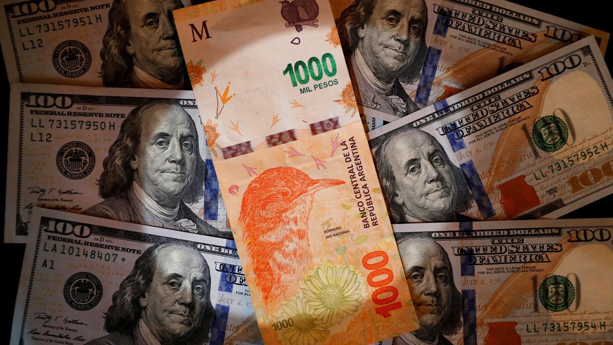 A one thousand Argentine peso bill sits on top of several one hundred U.S. dollar bills