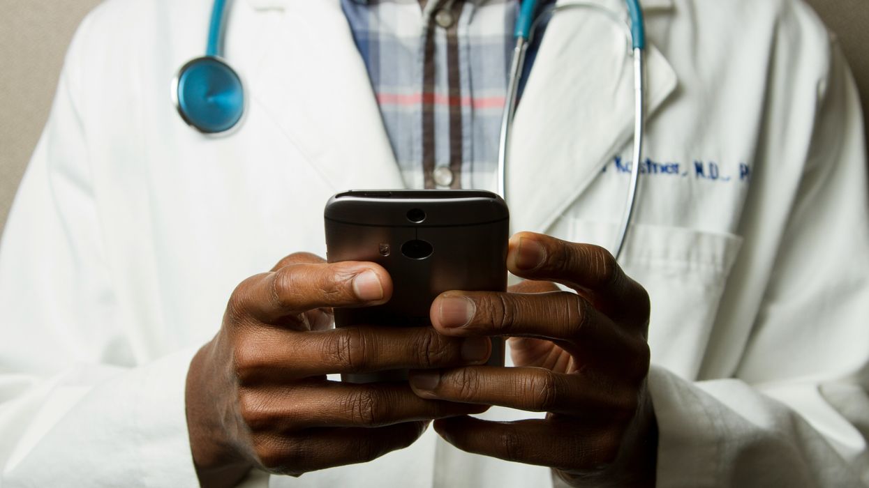 A person in a doctor's gown with a green stethoscope and a phone.
