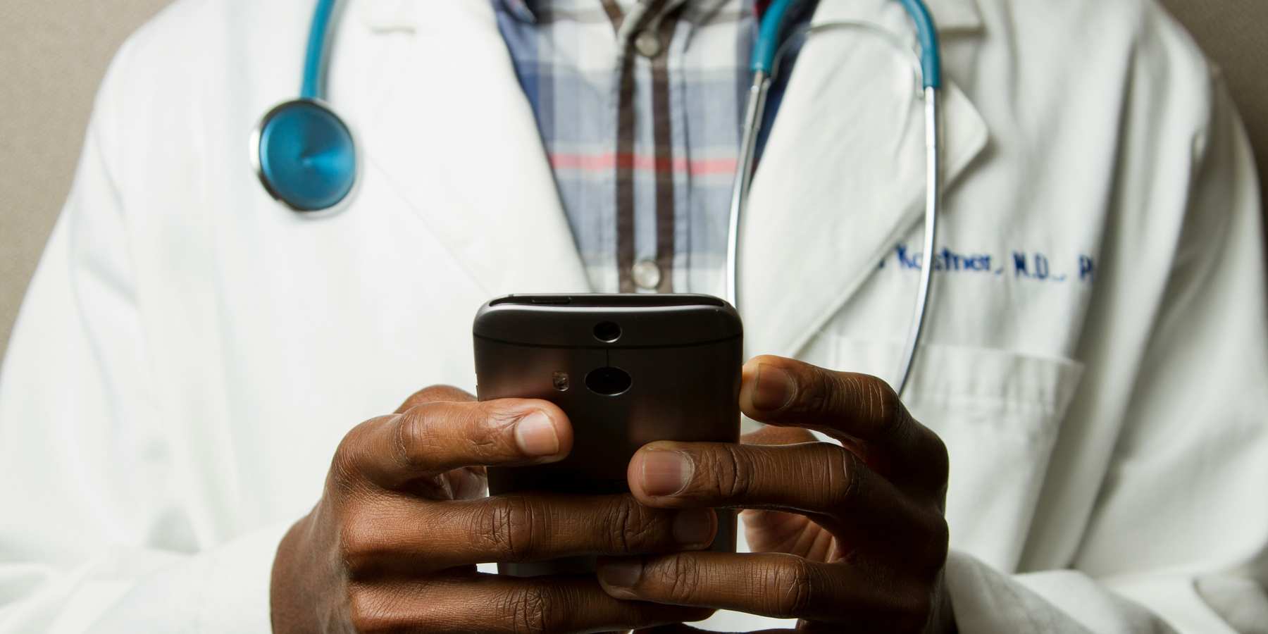 A person in a doctor's gown with a green stethoscope and a phone.