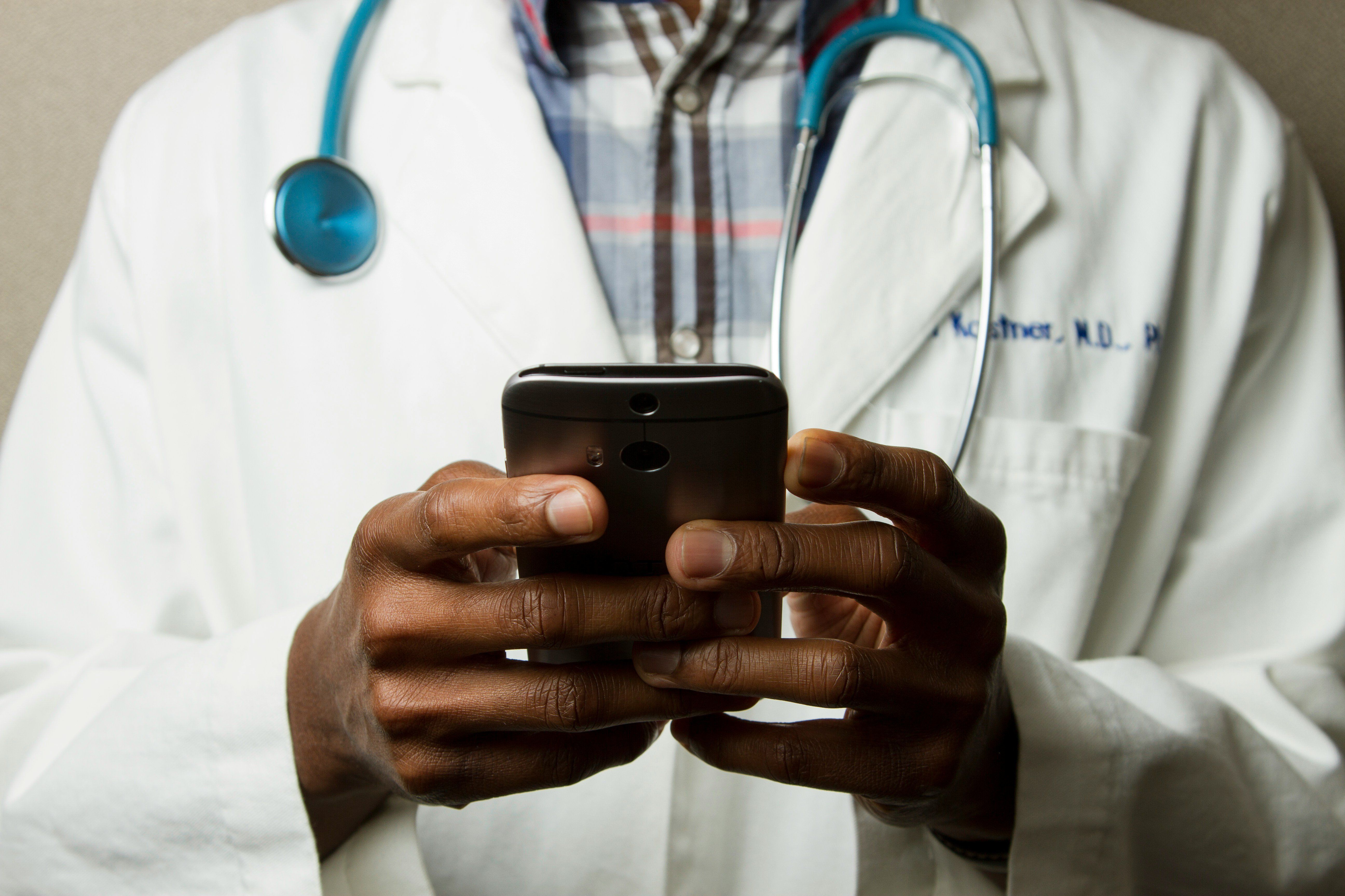 A person in a doctor's gown with a green stethoscope and a phone.