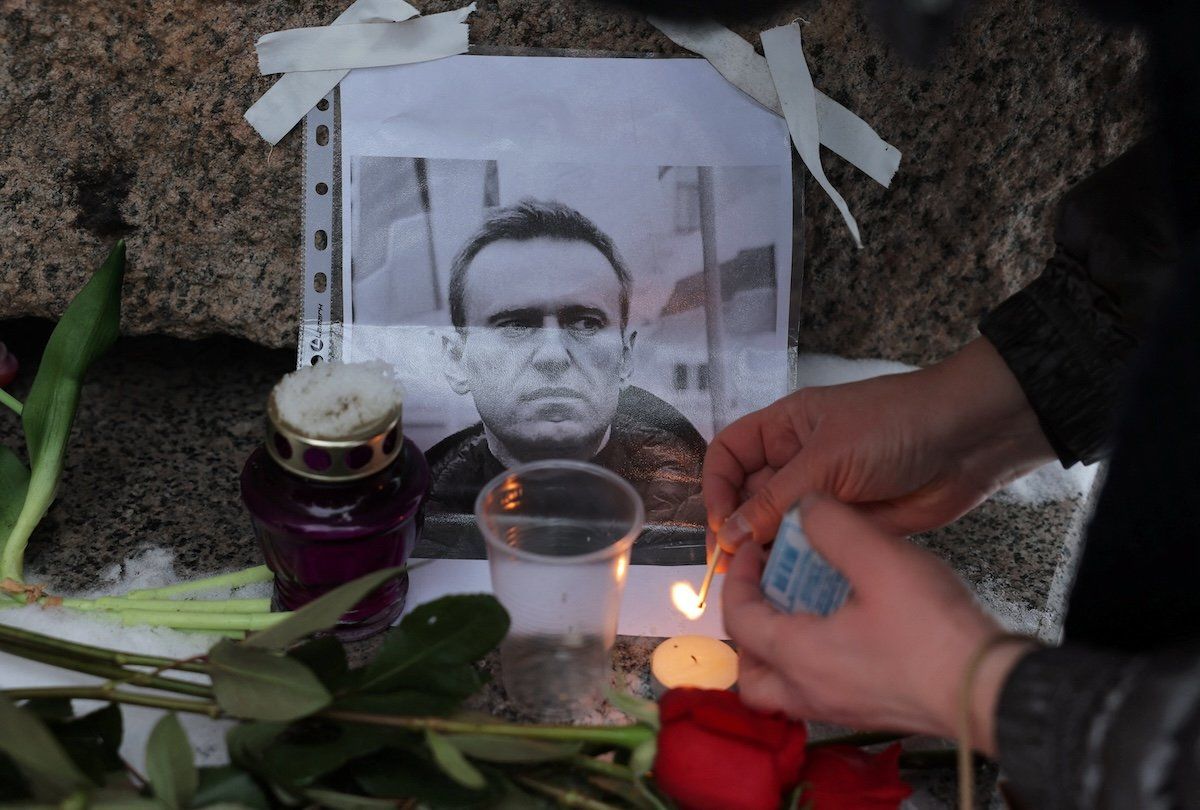 A person lights a candle next to a portrait of Russian opposition leader Alexei Navalny at the monument to the victims of political repressions following Navalny's death, in Saint Petersburg, Russia, on Feb. 16, 2024. ​