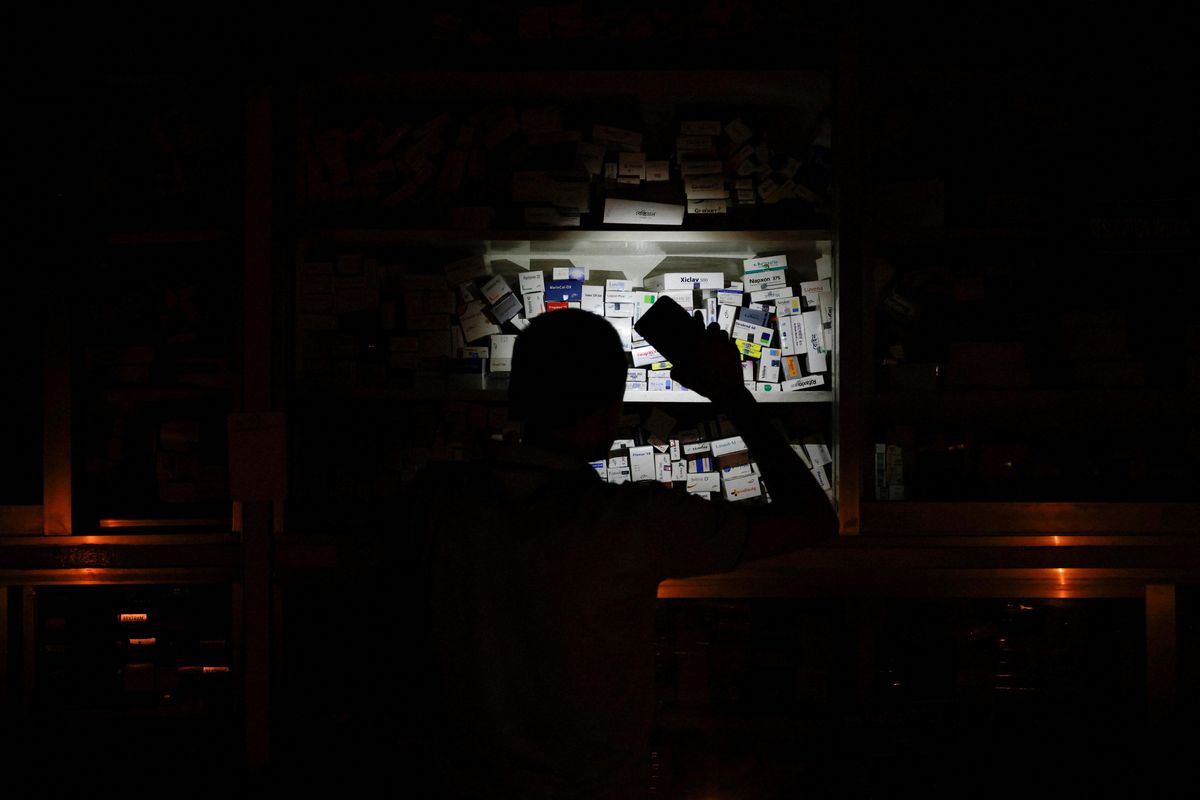 A pharmacist uses his phone light to serve customers during a nationwide blackout in Dhaka.