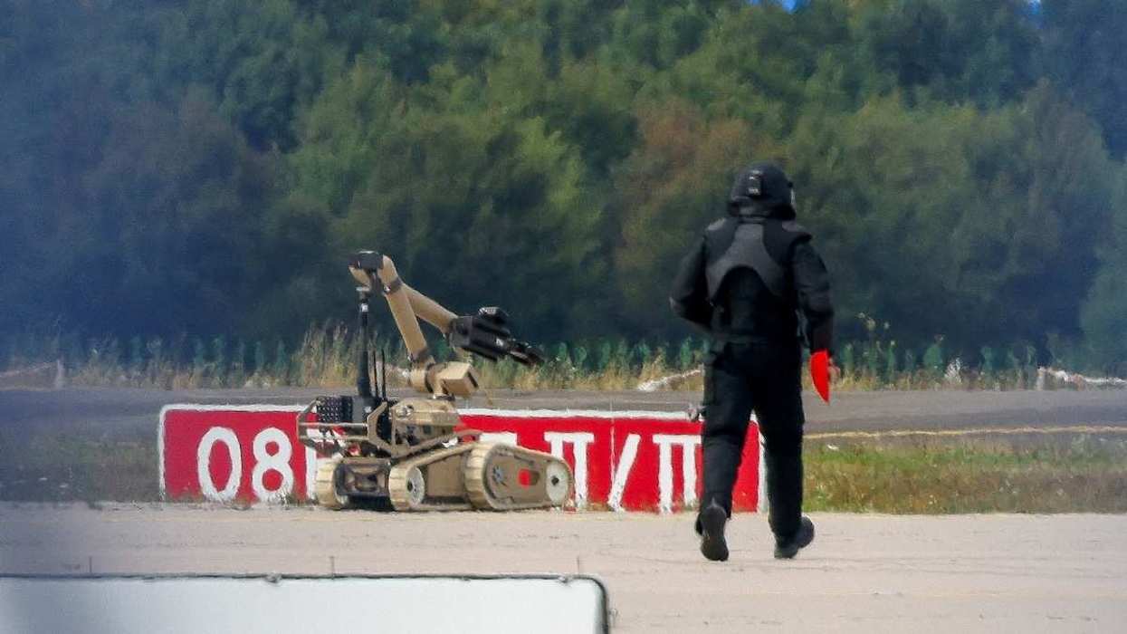 A police officer in protective clothing walks next to an explosive-disarming robot (EOD) at Leipzig/Halle Airport.