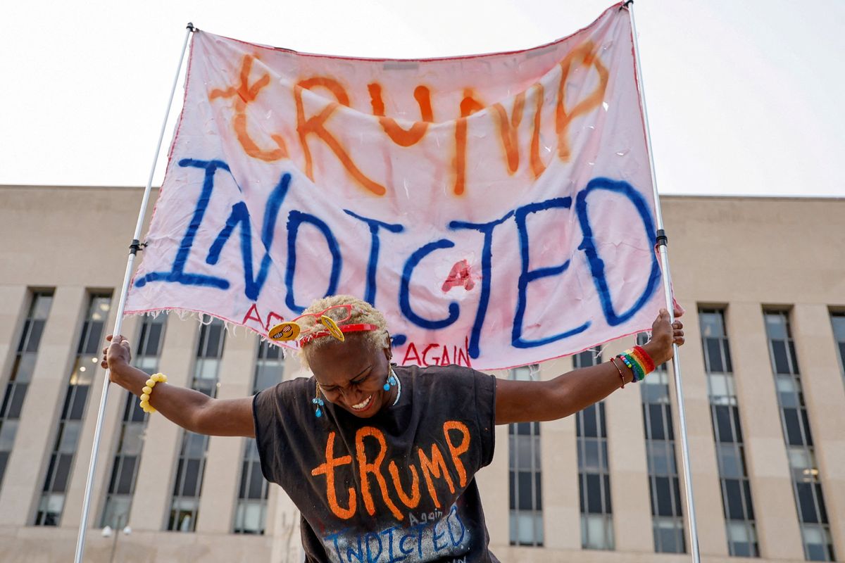 A protester holds a banner that says "Trump indicted." 