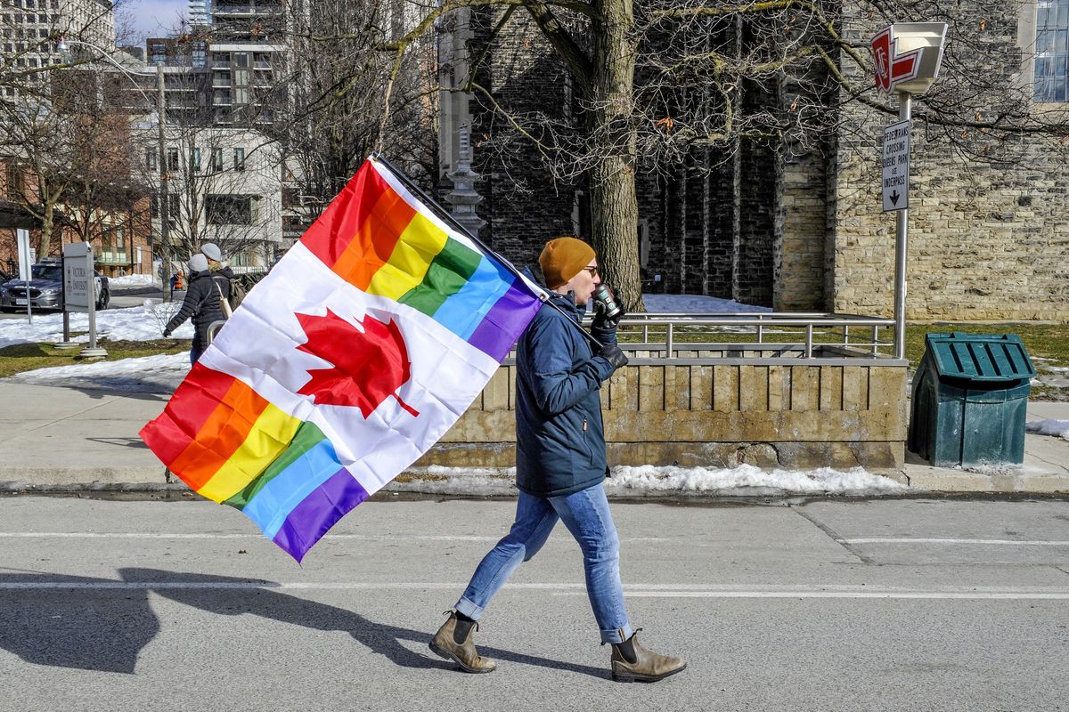 A protester is seen carrying a Canadian rainbow flag.