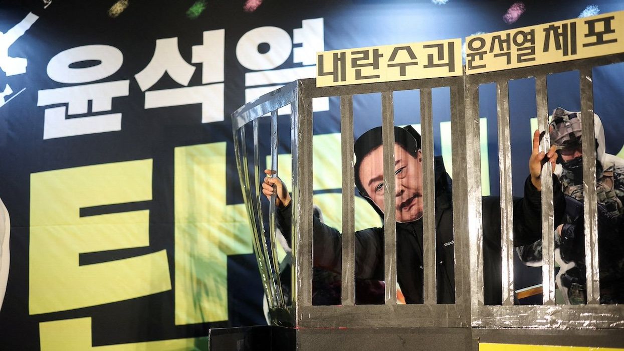 A protester wears a South Korean President Yoon Suk Yeol mask while holding a representation of prison bars, during a rally calling for the impeachment of the South Korean President, who declared martial law, which was reversed hours later, in front of the National Assembly in Seoul, South Korea, December 11, 2024.