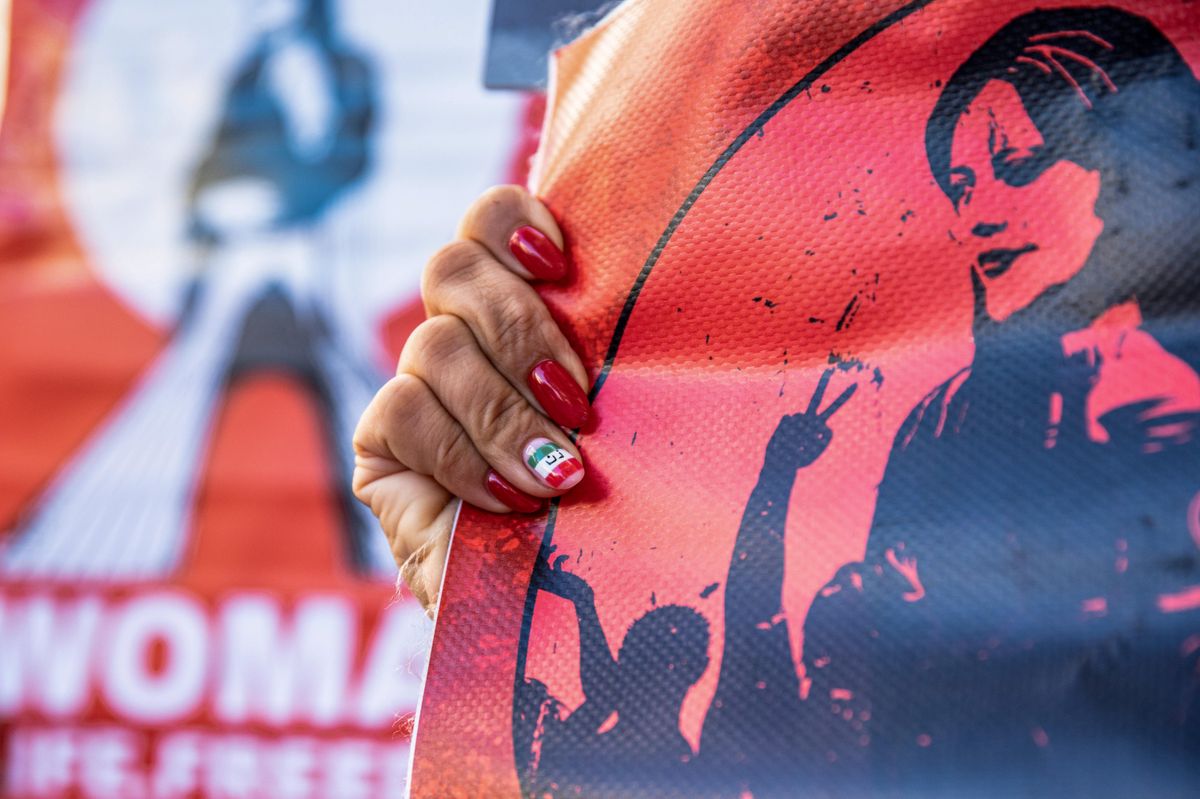 A protester with vanished nails in Iranian flag holds a portrait of Mahsa Amini. 