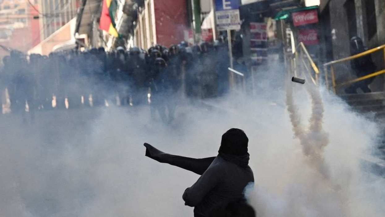 A protestor throws a tear gas canister back towards the police
