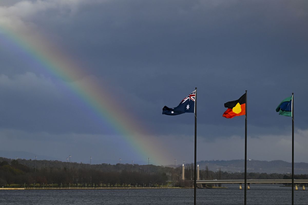 A rainbow is seen behind the Australian flag, the Indigenous flag and the flag of the Torres Strait Islands in Canberra, Friday, July 28, 2023.