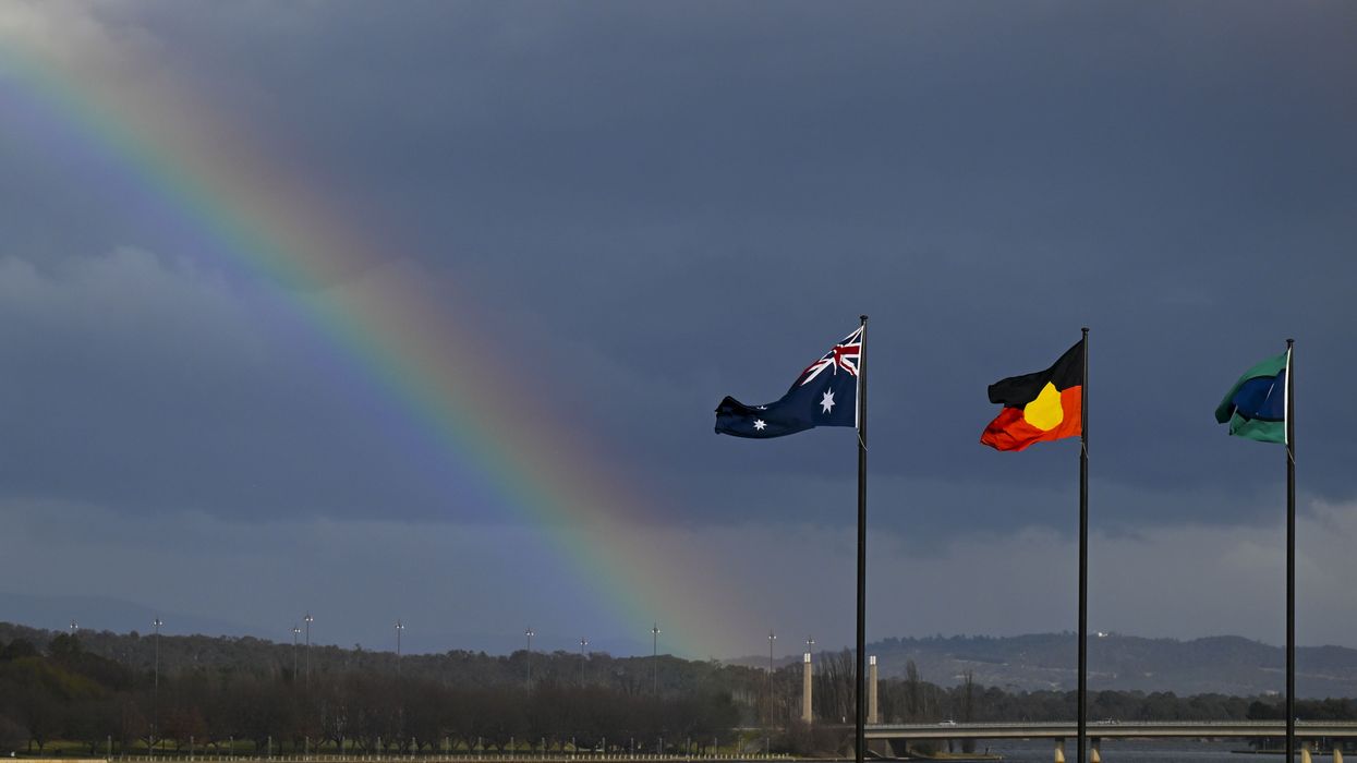 A rainbow is seen behind the Australian flag, the Indigenous flag and the flag of the Torres Strait Islands in Canberra, Friday, July 28, 2023.