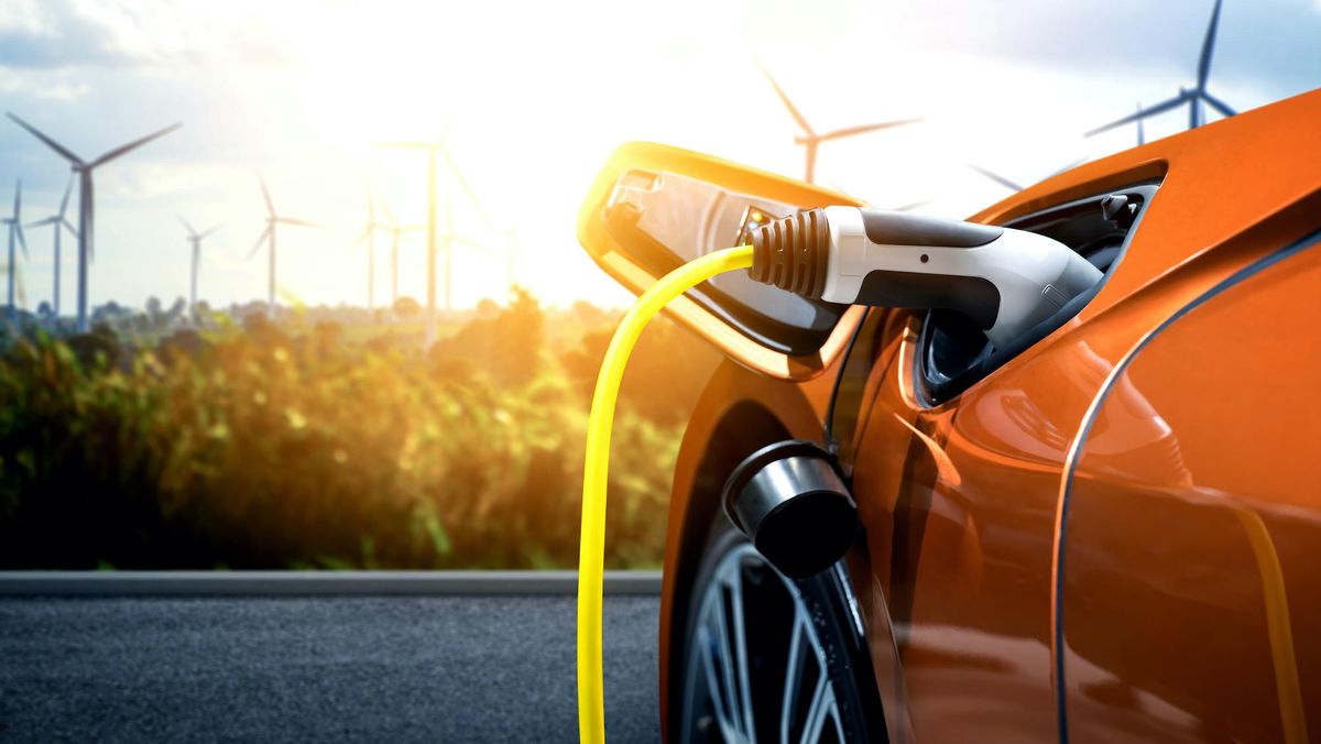 A red car being charged in the foreground with wind turbines in the background