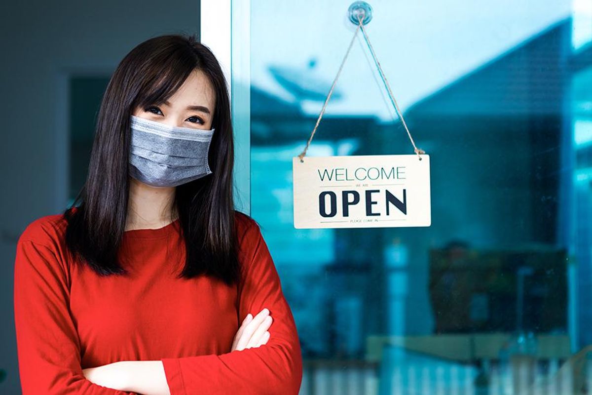 A small business owner in front of a business with a "welcome - open" sign
