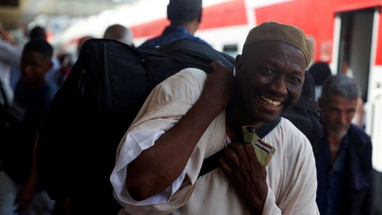 A Sudanese man smiles while carrying his luggage, as families displaced by conflict between the Sudanese Armed Forces and the Rapid Support Forces (RSF) crowd at Cairo's main station to board a free train with a voluntary return coordinated by the Egyptian government to Aswan, where buses will take them back to their homes in Khartoum, in Cairo, Egypt July 28, 2025.