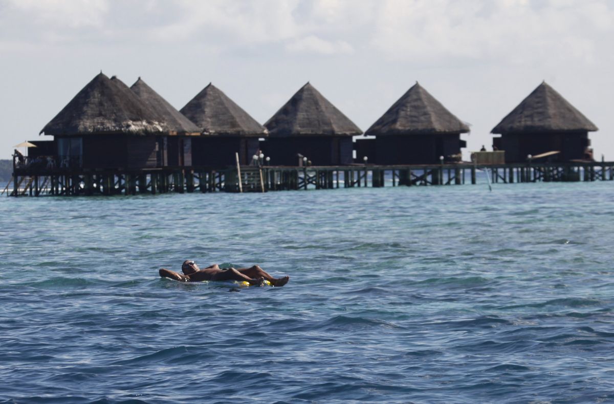 A tourist floats in front of huts at a resort island at the Male Atoll